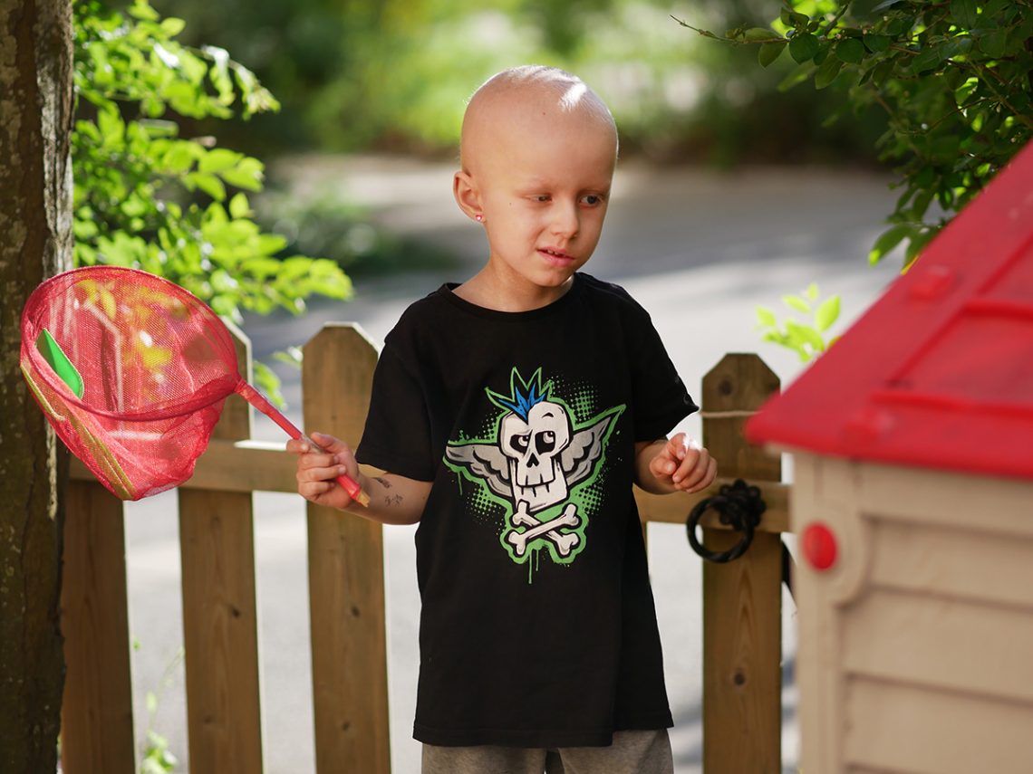 Elis står på uteplatsen med en håv i handen och en liten låtsasjuvel fastklistrad på örsnibben så att det ser ut som att han har ett örhänge