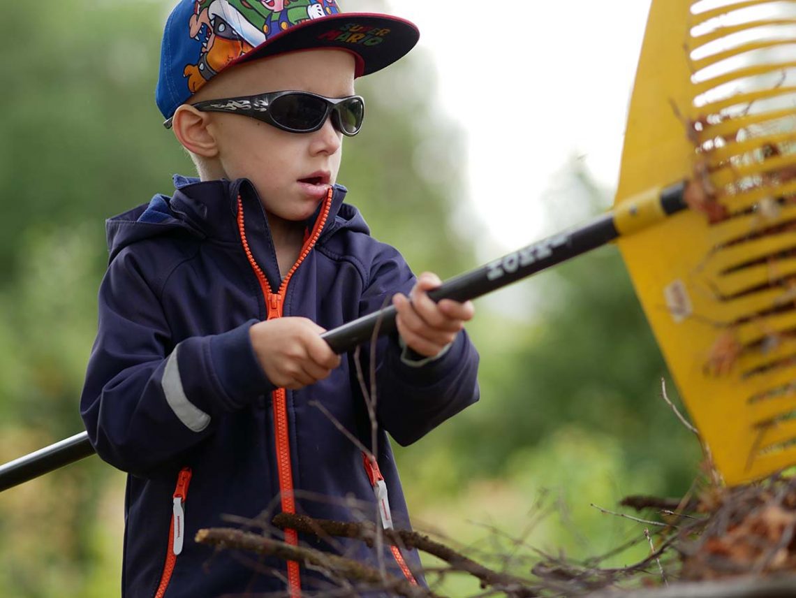 Folke och Elis vid skottkärran full av ris och torra löv