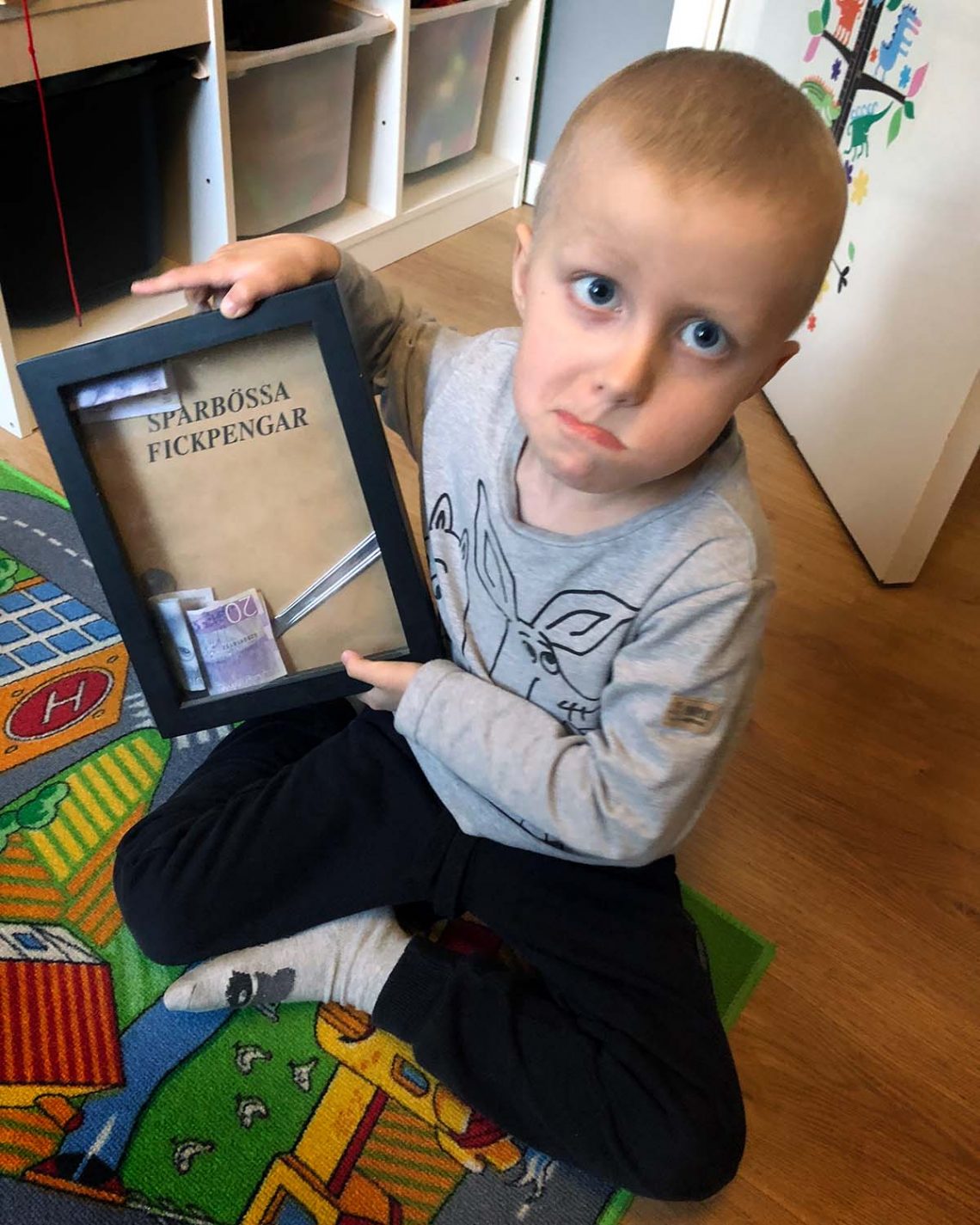 Elis sitter på golvet med sin sparbössetavla: han försökte peta ut ett mynt med en bordskniv men kniven ramlade in i tavlan
