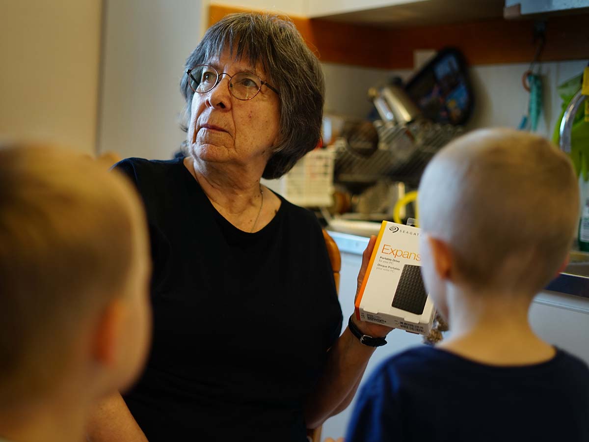 Folke och Elis tittar på och farmor håller upp hårddisken hon just fick i present