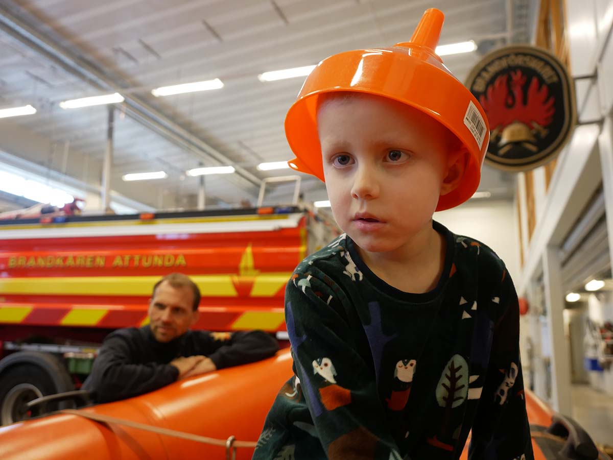 Elis sitter i brandkårens gummibåt och har satt en tratt på huvudet