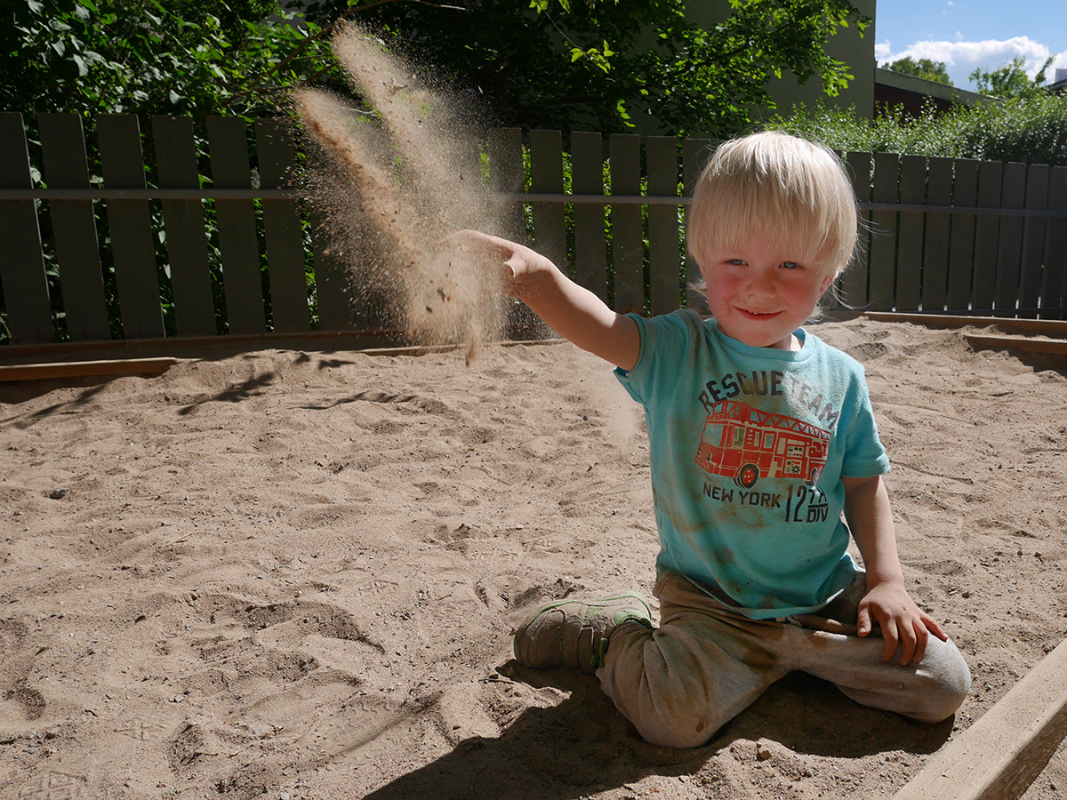Elis kastar en näve grus i sandlådan på förskolan, juni 2015