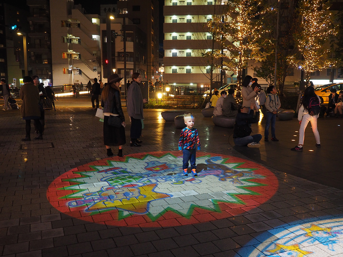 Treårige Elis står i projektionsbilden på trottoaren i Tokyo