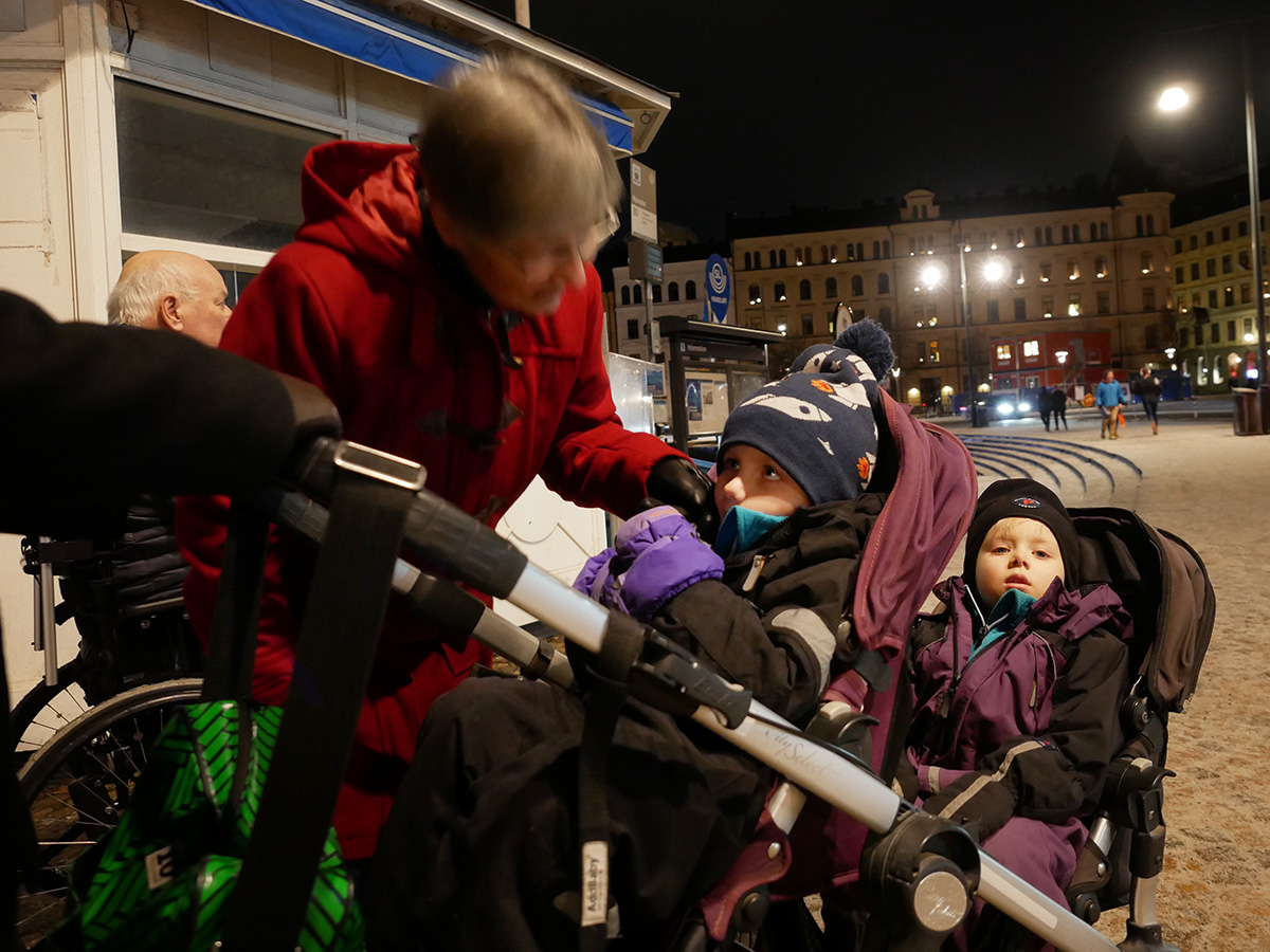 Elis och Folke sitter i syskonvagnen ute på stan, och mormor klappar Elis på kinden.