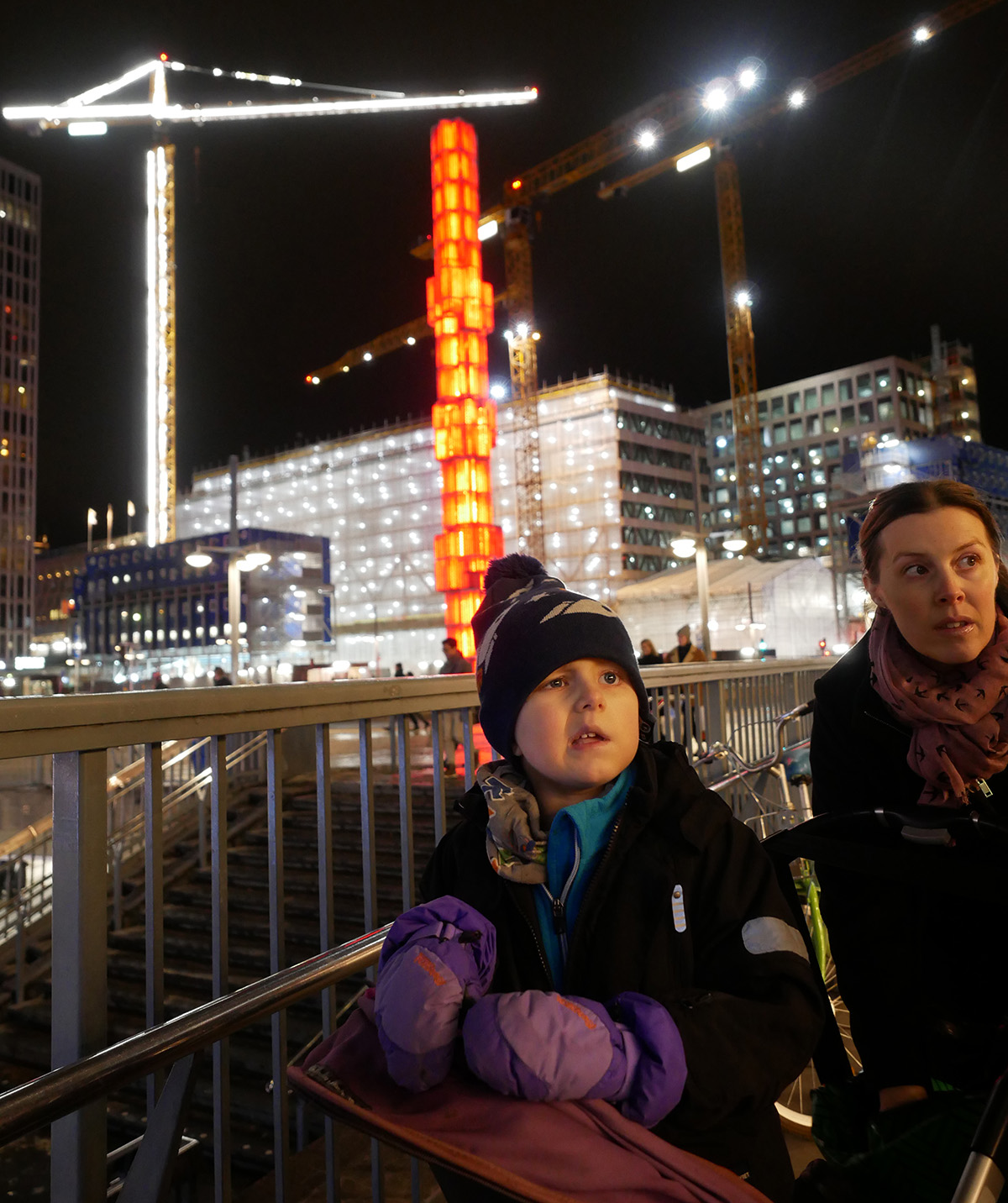 Elis och mamma ute på stan med en rödupplyst Sergels Torgs-pinne i bakgrunden
