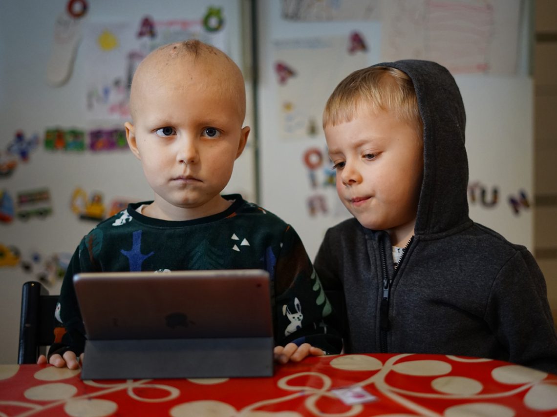 Elis och Folke sitter vid köksbordet och kollar på en iPad.