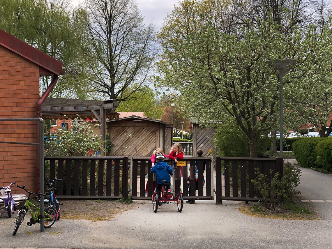 Elis med sin nya lastcykel utanför förskolans grind, med barn som tittar på