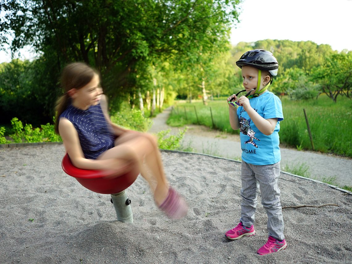 Lilly snurrar runt i en snurrkopps-leksak på lekplatsen medan Elis tittar på
