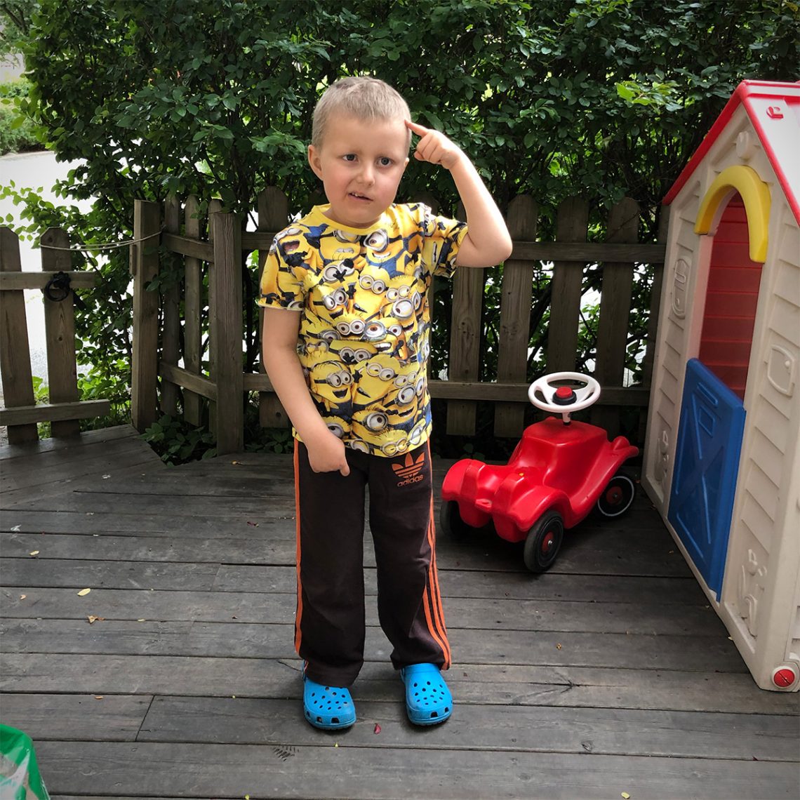 Elis på uteplatsen, i Minionerna-tröja, blå Foppatofflor och bruna Adidasbyxor