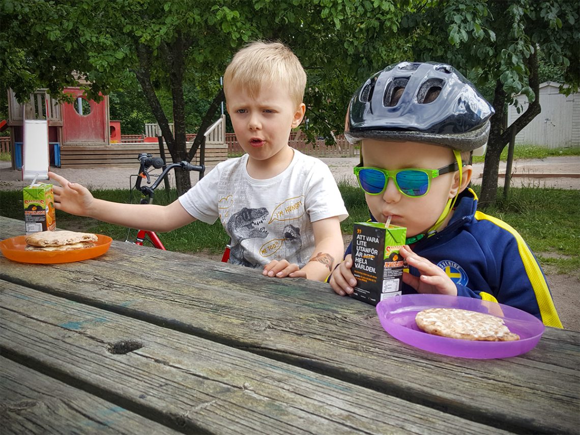 Folke och Elis sitter och äter medhavda mackor och dricker Smakis med lastcykeln i bakgrunden