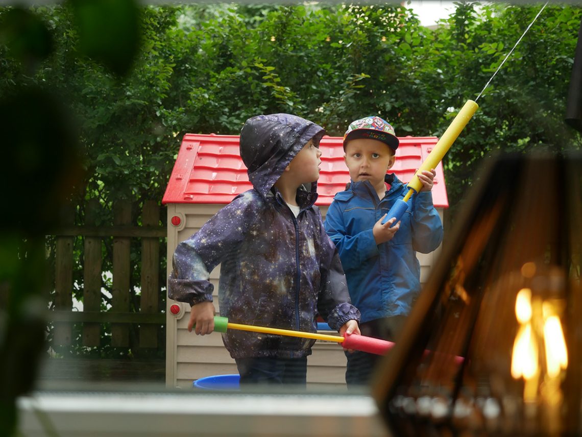 Folke och Elis leker med vattensprutor i regnet på uteplatsen