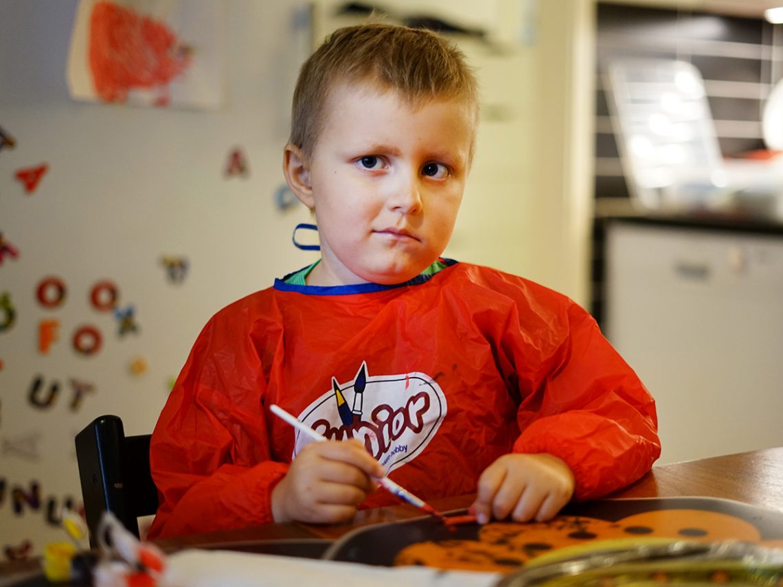 Elis Wikmark pysslar hemma vid köksbordet, iklädd ett rött målarförkläde