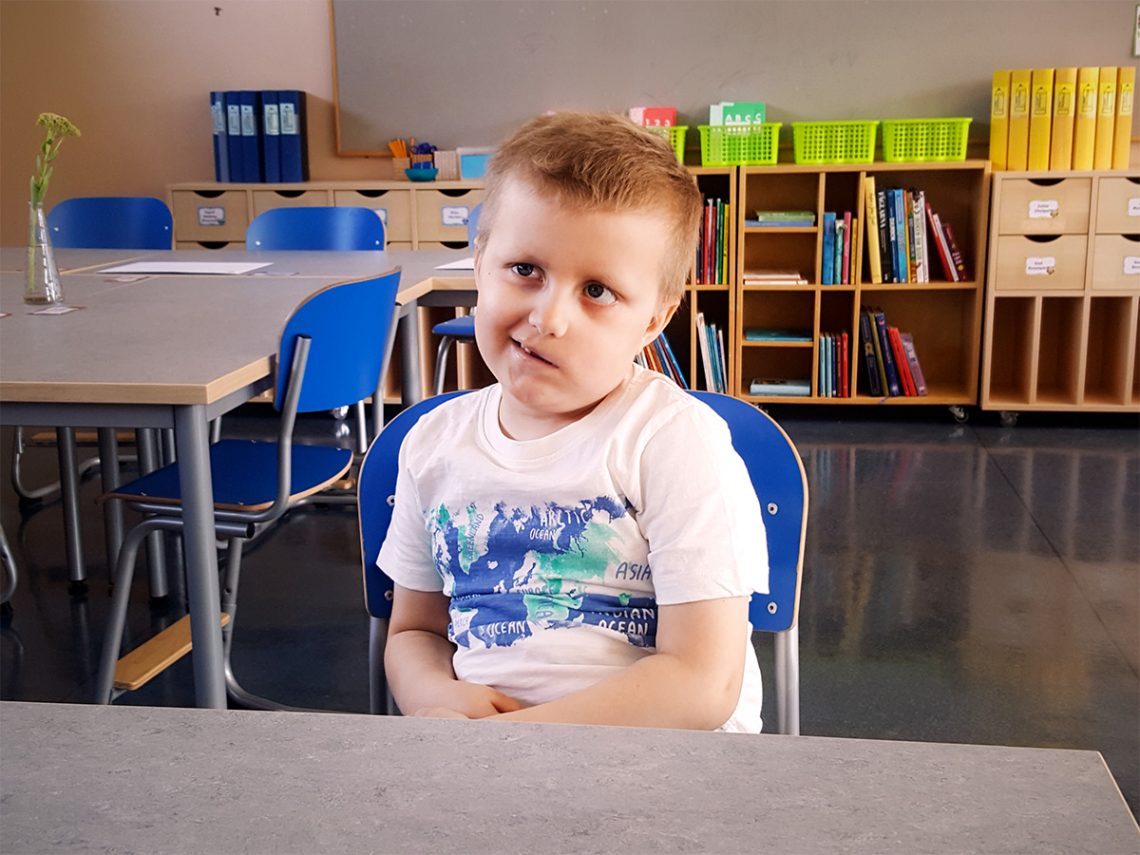 Elis sitter i skolbänken och ler på sitt karaktäristiskt sneda vis.