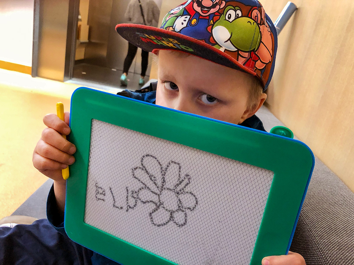 Elis sitter nere i sjukhusgaraget och väntar på taxin, med sin nya ritplatta där han skrivit "Elis" och ritat en blomma.