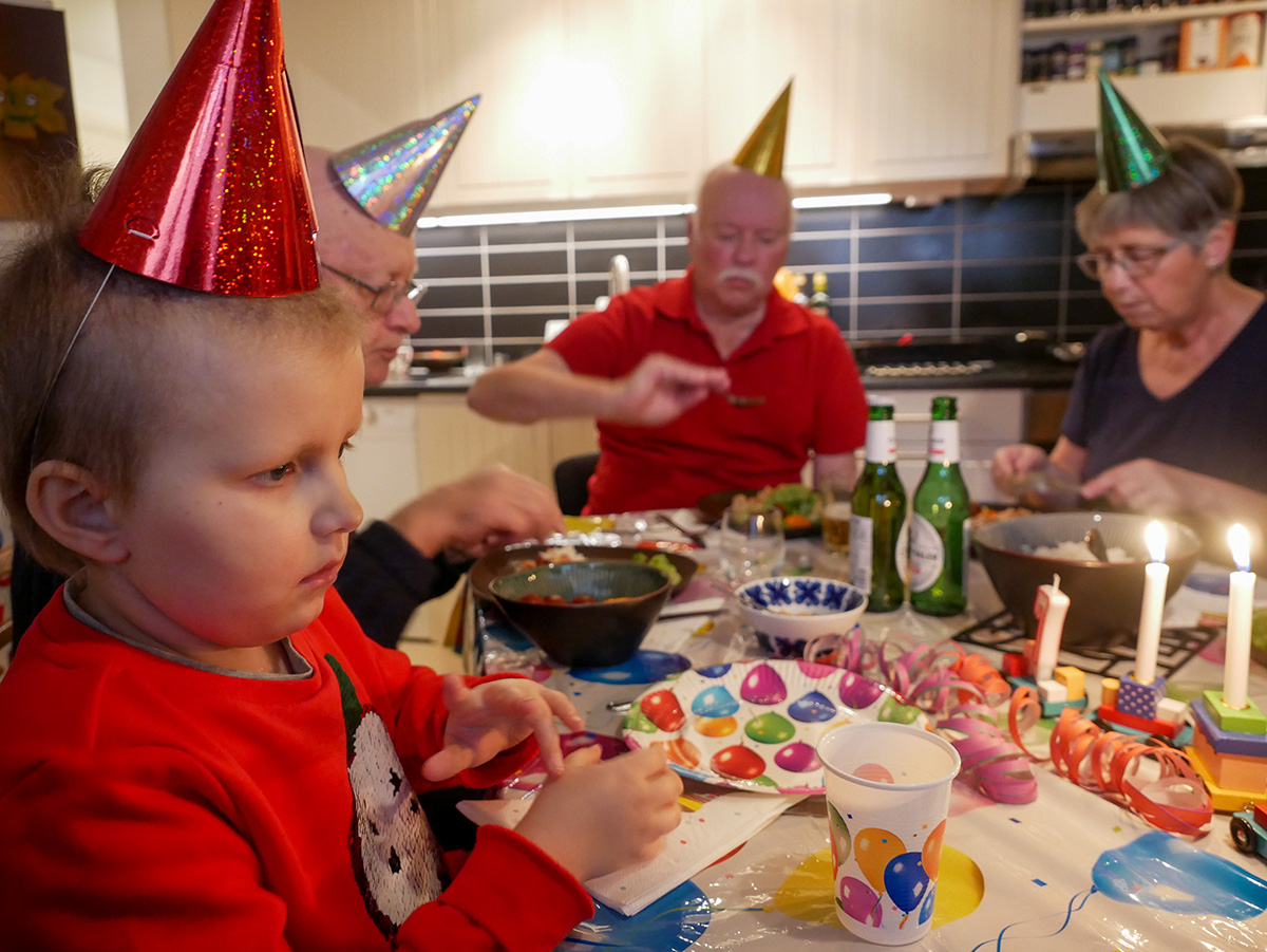 Elis, farfar, morfar och mormor vid kalasbordet med partyhattar på