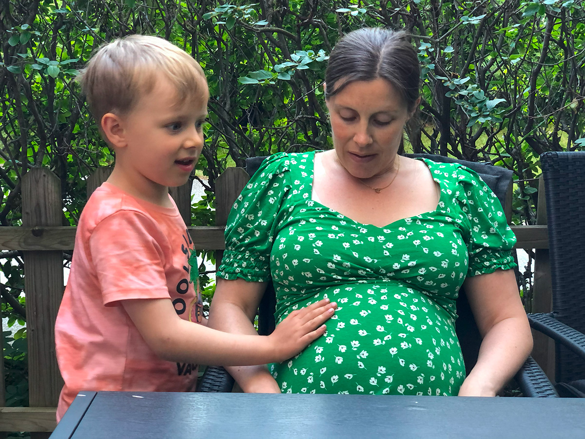 Folke lägger handen på mammas mage för att känna om lillebror sparkar.