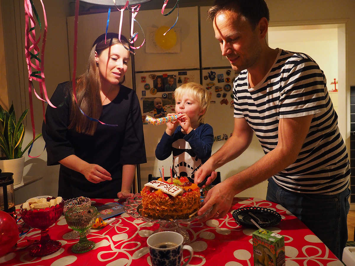 Elis blåser i en flärp medan mamma och pappa ställer fram fyraårstårtan